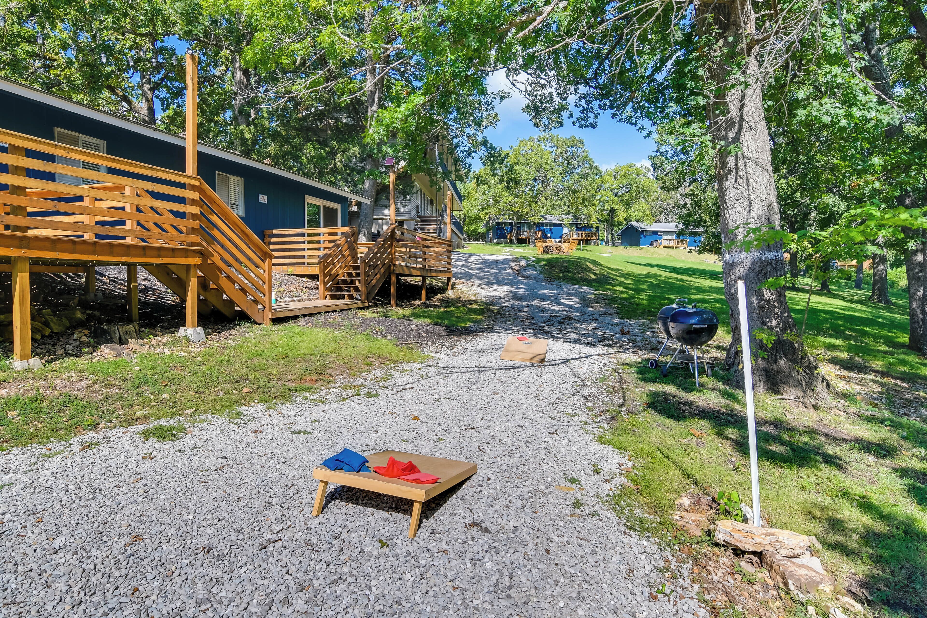 Eine Holzterrasse, die zu einem Gebäude mit Treppe, Kiesweg und Grill führt.