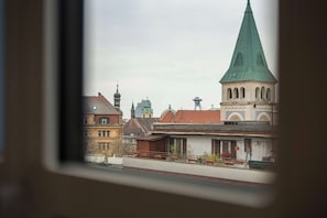 A view of a building with a green spire and a clock tower, through a window with a wooden frame. - The Heart of Shopping & City Life (Bratislava)