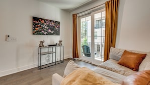 A living room with a sofa, a coffee table, a painting, and a window with curtains. - 1 Mi Decatur Square New Condo Walkable to Marta (Decatur)