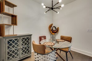 A dining area with a glass table, two chairs, a cabinet with glass doors, a decorative wall piece, and a modern chandelier.