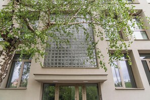 Eine Gebäudefassade mit einem großen Fenster, mehreren kleineren Fenstern und einem Baum mit grünen Blättern.