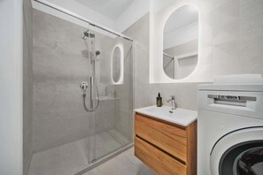 Ein modernes Badezimmer mit einer gläsernen Duschkabine, einer Bosch Waschmaschine und einem Holzwaschtisch.