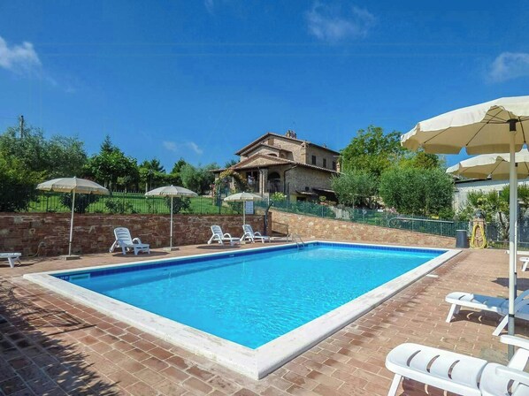 A rectangular swimming pool with a brick border, surrounded by white lounge chairs and umbrellas. - Apartment near Lake Trasimeno with view (Castiglione del Lago)