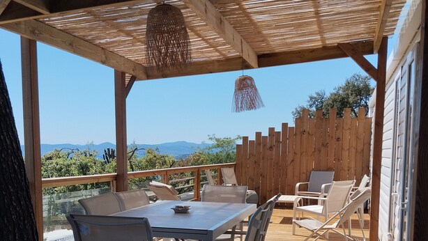 Une terrasse extérieure couverte, dotée d’une table et de chaises, d’un luminaire suspendu et offrant une vue sur les montagnes lointaines.