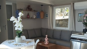Un espace de vie compact comprenant une table à manger, des chaises, un canapé, une petite table basse, un coin cuisine avec une cuisinière et une fenêtre avec des rideaux.