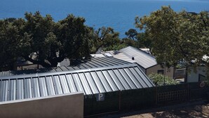 Une vue côtière avec un bâtiment dont le toit est fait de tôle ondulée, un panneau de signalisation indiquant un parking et des arbres au premier plan.