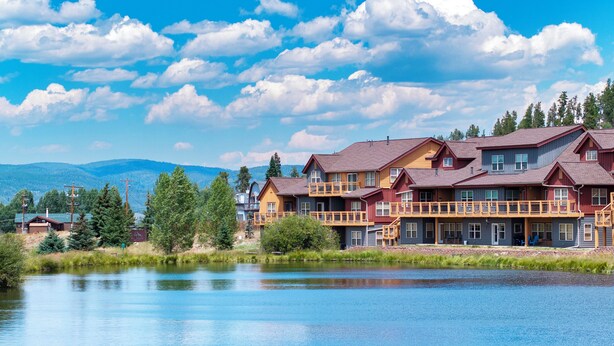 Ein Hotel am Seeufer mit mehreren Gebäuden, einer Holzterrasse und Blick auf See und Berge.