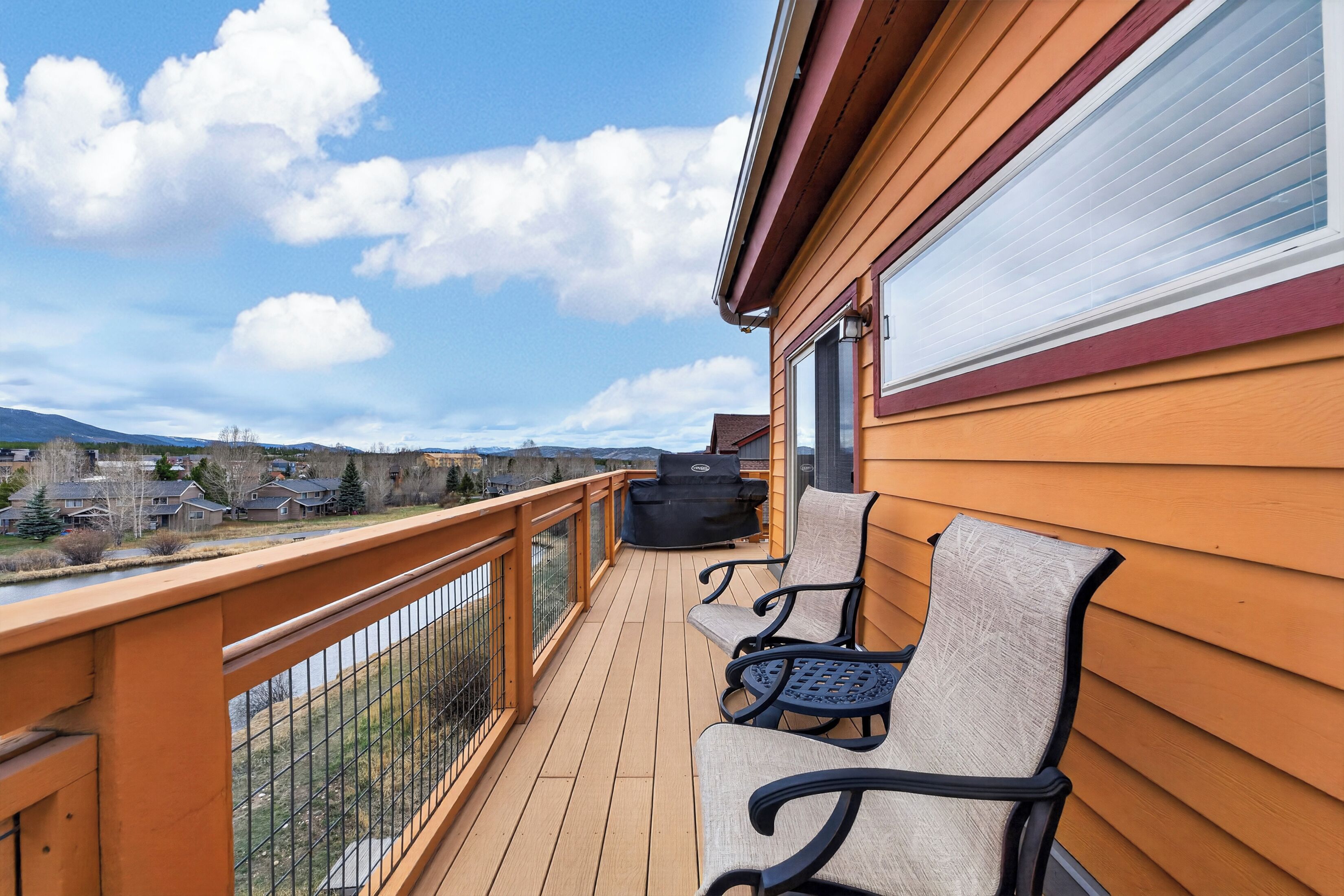 A wooden deck with outdoor furniture, a view of a residential area, and a clear sky.