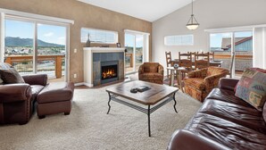 Ein geräumiges Wohnzimmer mit Kamin, Ledersofas und einem Balkon mit Bergblick.