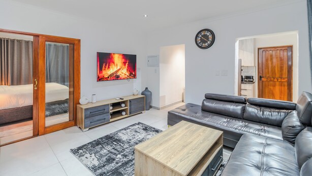 Uma sala de estar moderna com um sofá, uma mesa de centro, uma televisão e uma porta de vidro deslizante que dá para um quarto.