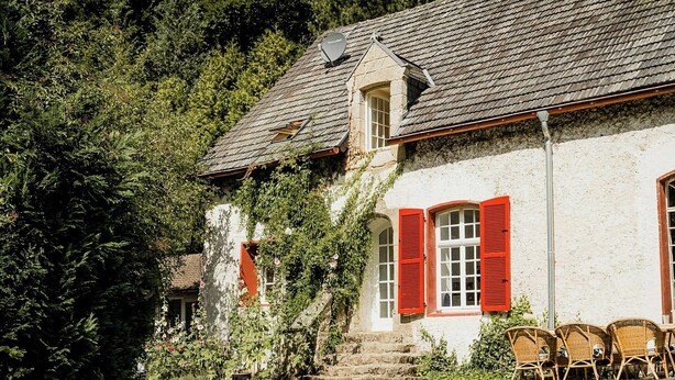 A stone building with red shutters, a staircase, and wicker chairs outside. - Experience original nature in the steward's house (Kall)