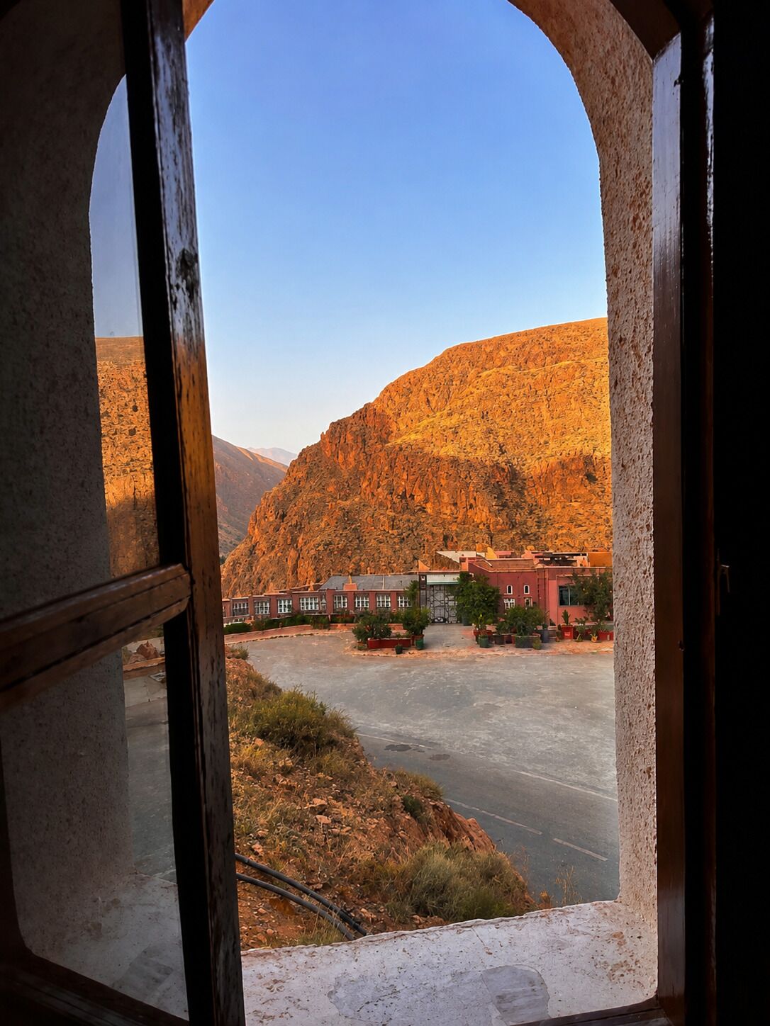 A view through an arched doorway of a building with a parking lot and a mountainous landscape in the background.