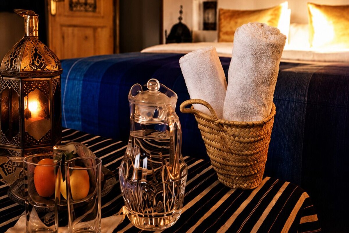 A neatly arranged table with a lantern, a glass pitcher, and glasses with fruits. A basket with towels is also visible.