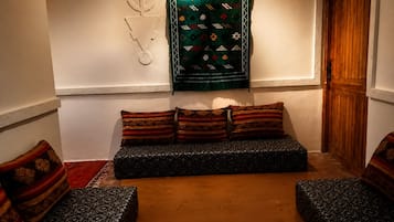 A cozy room with a sofa set, patterned cushions, a decorative wall hanging, and a wooden door.