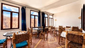 A dining area with tables and chairs, large windows with curtains, and a view of a mountainous landscape.