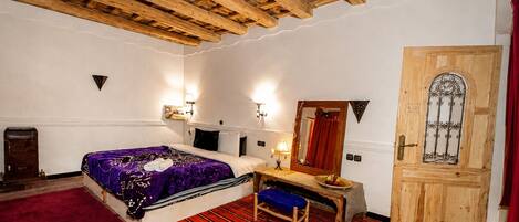A room with a bed, a desk, a chair, a wooden door, and a red carpet.