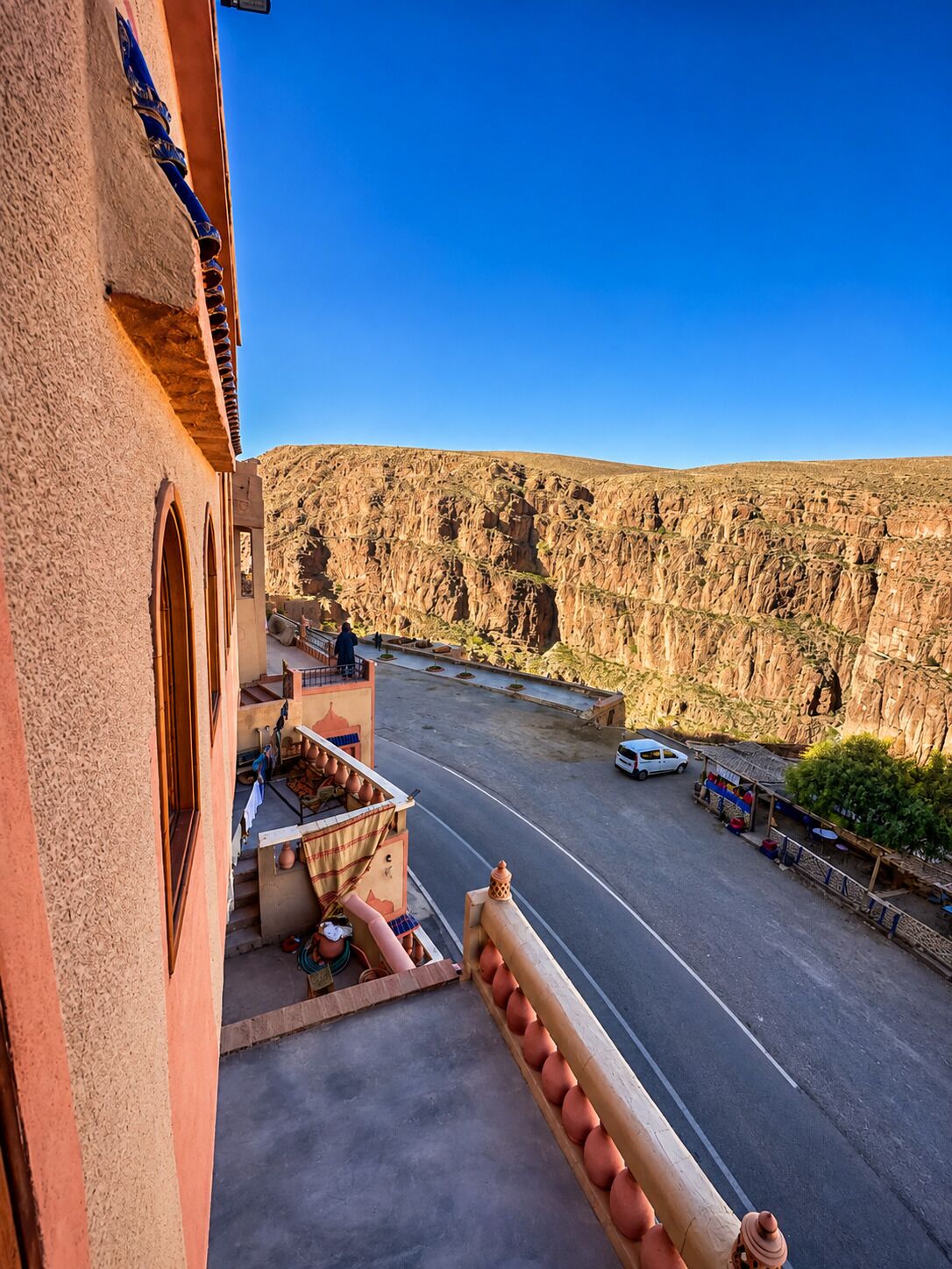 A building with a balcony overlooking a road and a rocky cliff.