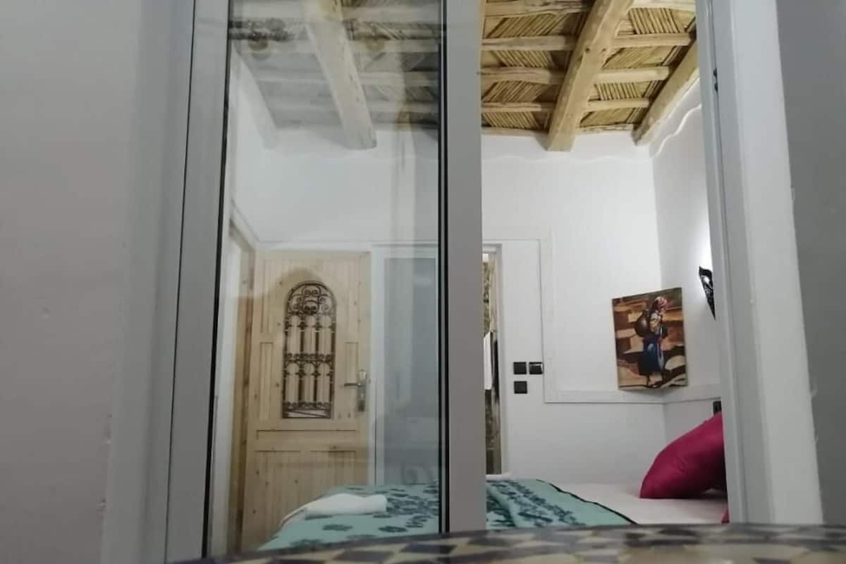 Una habitación con una cama, una puerta y un techo con vigas de madera.