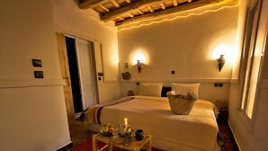 A cozy hotel room with a bed, bedside lamps, a small table with a candle, and a basket of items. - Riad Bleu Afriqua (Ait Sedrate Jbel El Soufla)