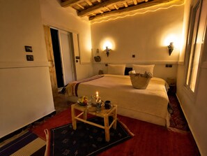 A cozy hotel room with a bed, bedside lamps, a small table with a candle, and a basket of items.