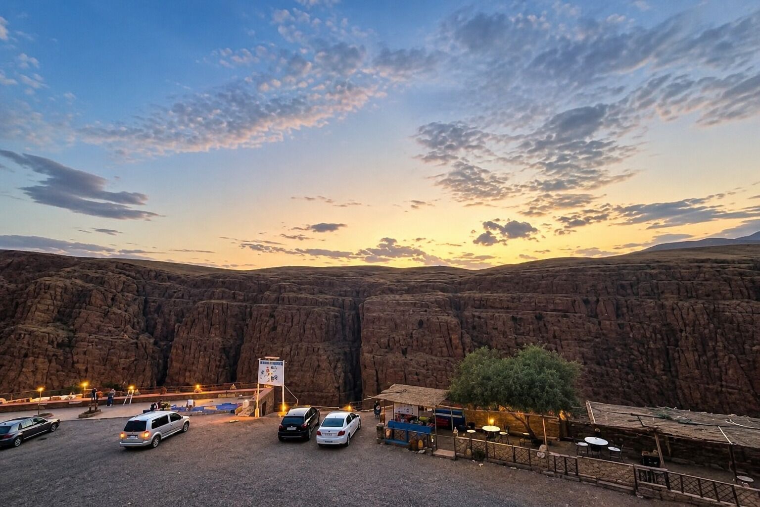 A parking area with vehicles, a sign, and a small outdoor seating area with tables and chairs.