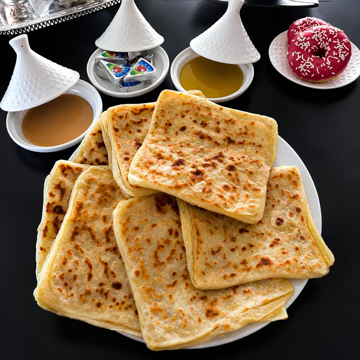 A plate of flatbreads with two small bowls of dipping sauces and a plate of donuts.