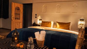 Ett hotellrum med en stor sÀng, en trÀdörr och ett nattduksbord med en lampa.