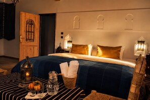 A hotel room with a large bed, a wooden door, and a nightstand with a lamp. - Riad Bleu Afriqua (Ait Sedrate Jbel El Soufla)