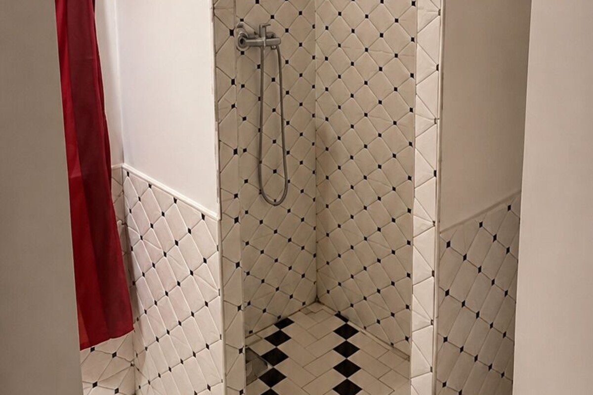 A bathroom with a shower area, white tiled walls, and a black and white checkered floor.