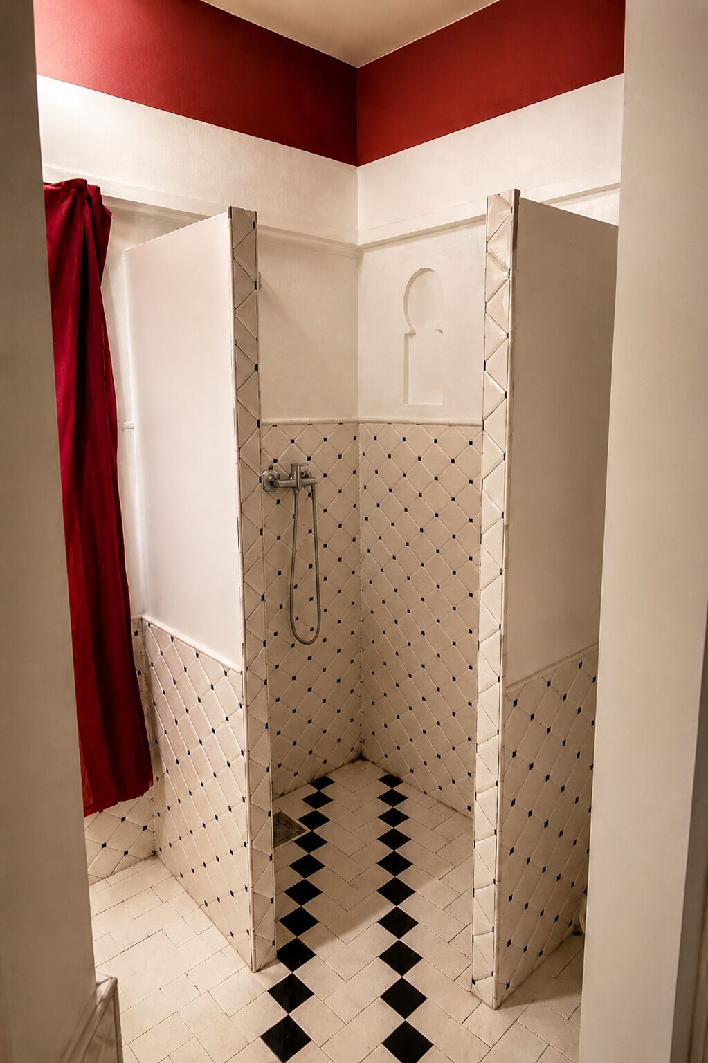 A bathroom with a shower, white walls, and a red towel hanging on the wall.