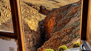 Vista desde una ventana a un paisaje montañoso con una carretera, un paño morado y unas botas negras sobre un alféizar de madera.