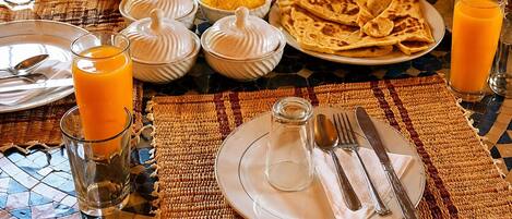 A breakfast setting with a table set for two, including plates, glasses, and a basket of bread.