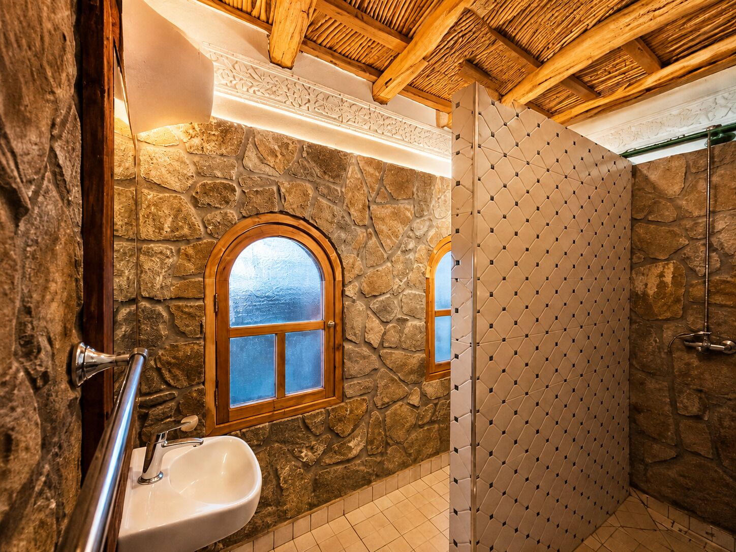 A bathroom with a stone wall, a wooden-framed window, a sink, and a shower area.