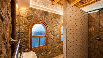 A bathroom with a stone wall, a wooden-framed window, a sink, and a shower area.