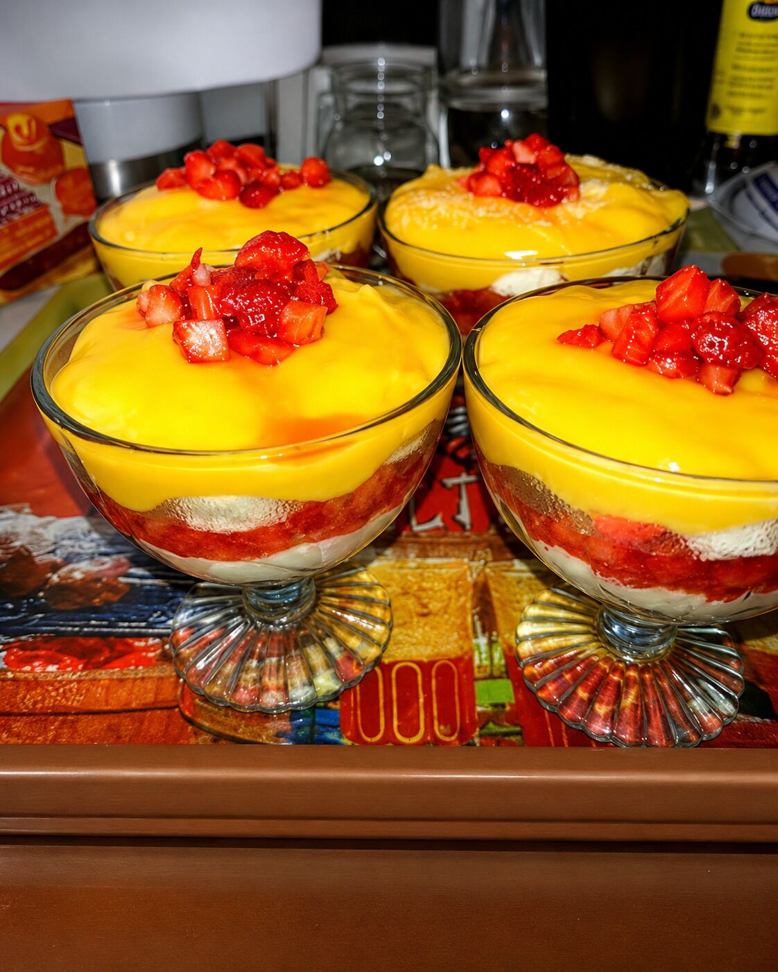 A dessert tray with three glass bowls containing layered fruit parfaits topped with strawberries.