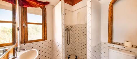A bathroom with a sink, toilet, shower, and a window.