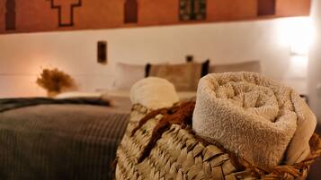 A bed with a woven basket containing towels, a wall with geometric patterns, and a bedside table with a vase.
