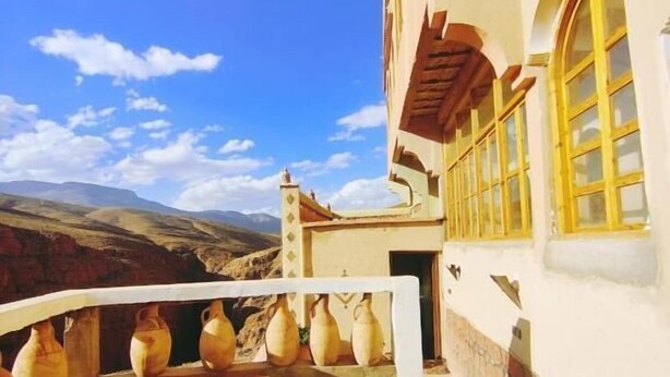 A building with a white exterior, yellow window frames, and a balcony with pottery. - Riad Bleu Afriqua (Ait Sedrate Jbel El Soufla)
