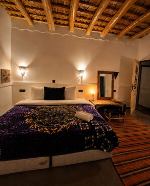 A hotel room with a bed, bedside lamps, a wooden ceiling, and a mirror.