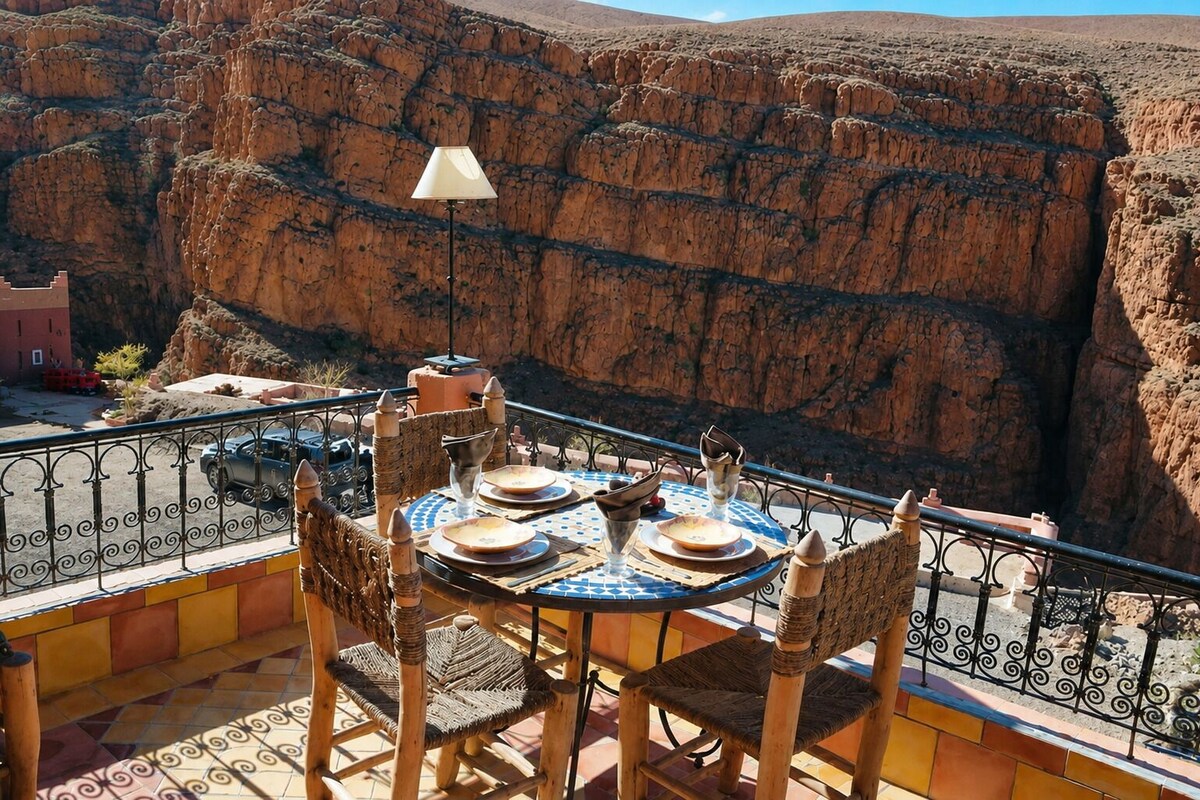 A dining table set with plates, glasses, and a lamp, overlooking a rocky canyon.