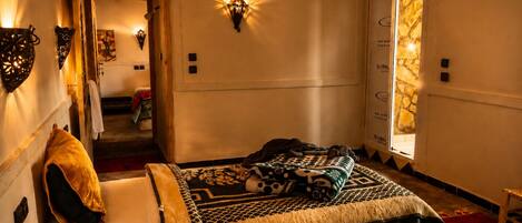 Habitación de hotel con cama, alfombra roja, puerta con diseño de piedra y luces fijadas a la pared.