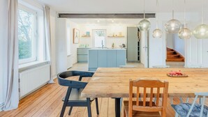 Eine moderne Küche mit einer zentralen Kochinsel, einem Holztisch und Pendelleuchten.