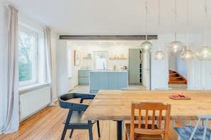 A modern kitchen with a central island, wooden dining table, and pendant lights. - Historic Villa in North Frisia (Ostenfeld)