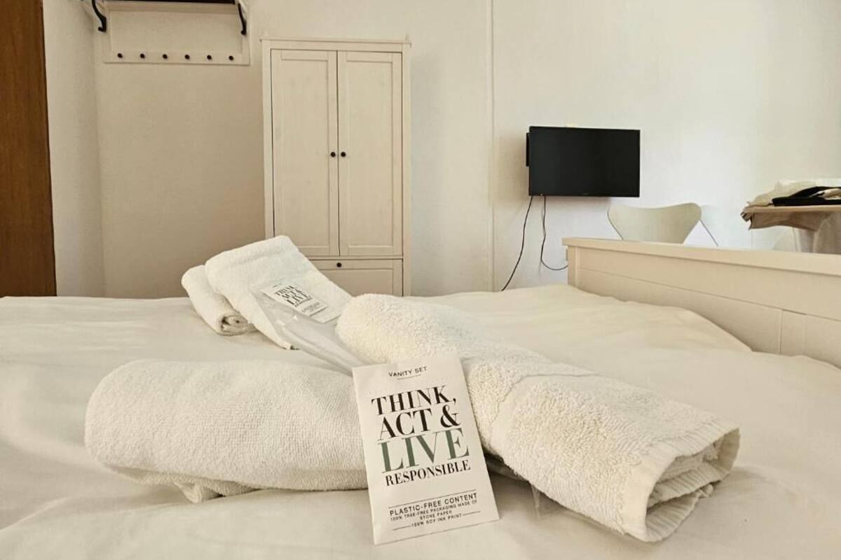 A hotel room with a bed, a TV, a wardrobe, and a towel with a message.