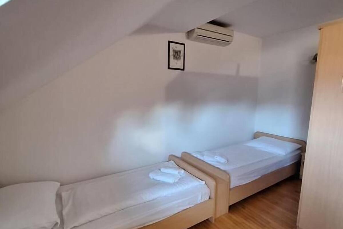 A small, single-room with two bunk beds, a wooden wardrobe, and a framed picture on the wall.