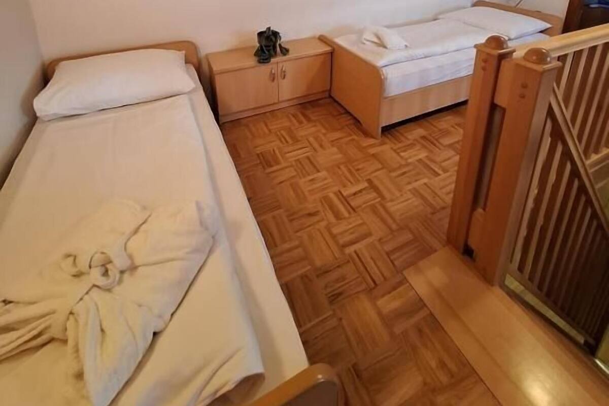 A small, single-bedroom room with a wooden floor, a bed, a nightstand, and a window.