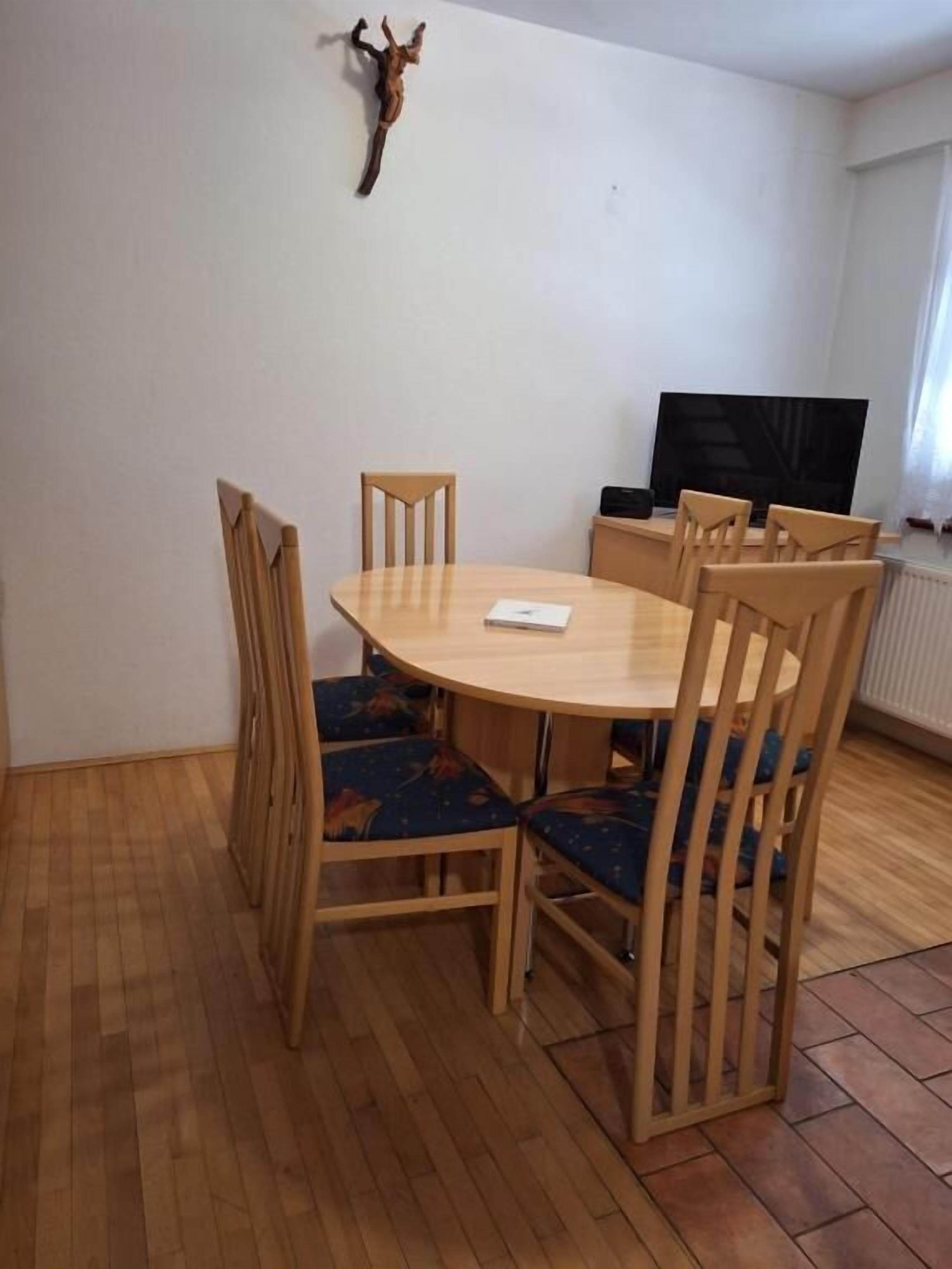 Ein Essbereich mit einem runden Tisch, sechs Holzstühlen und einem Fernseher auf einem Schrank.