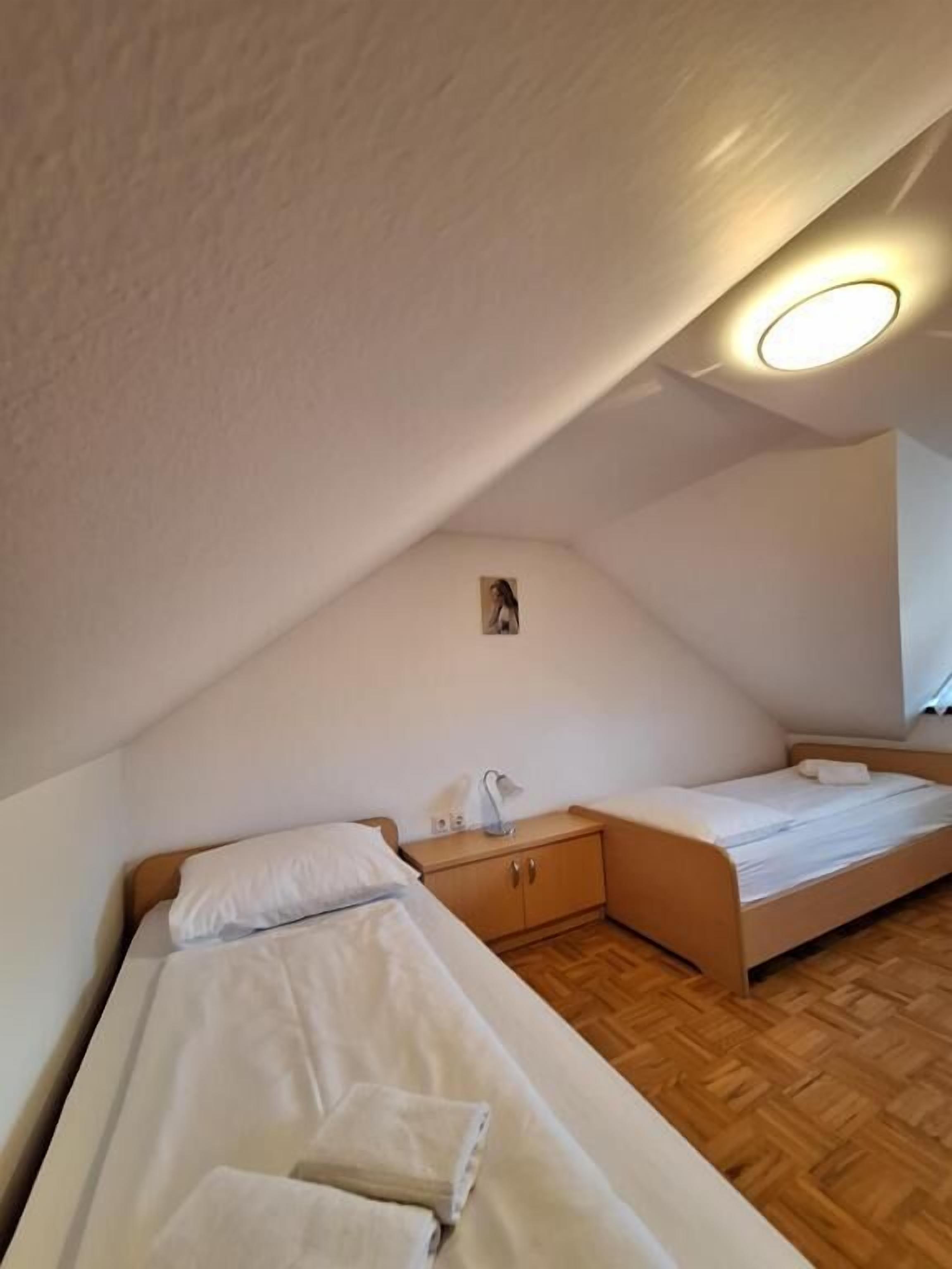 A small, cozy room with two beds, a wooden floor, a ceiling light, and a small cabinet.