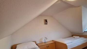 A small, cozy room with two beds, a wooden floor, a ceiling light, and a small cabinet.