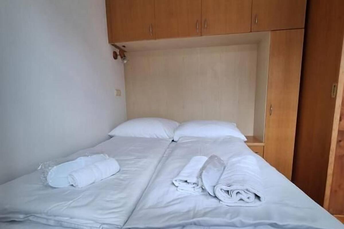 A single bed with white linens and towels, wooden headboard, and a wooden wardrobe.